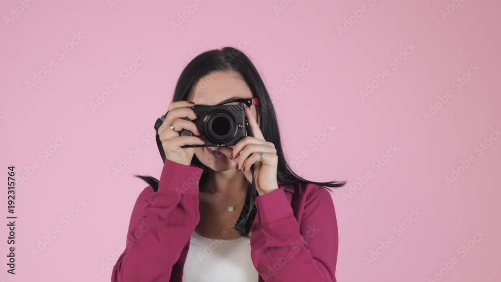 Young pretty brunette woman in pink shirt takes pictures with DSLR camera over colorful background in studio. Girl smiling, flirting and having fun as photographer. 4k Young pretty brunette woman in pink shirt takes pictures with DSLR camera over colorful background in studio. Girl smiling, flirting and having fun as photographer. 4k