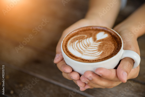 Woman hands holding cup of hot coffee latte cappuccino with heart shaped. Love, Wedding and Valentines day concept.