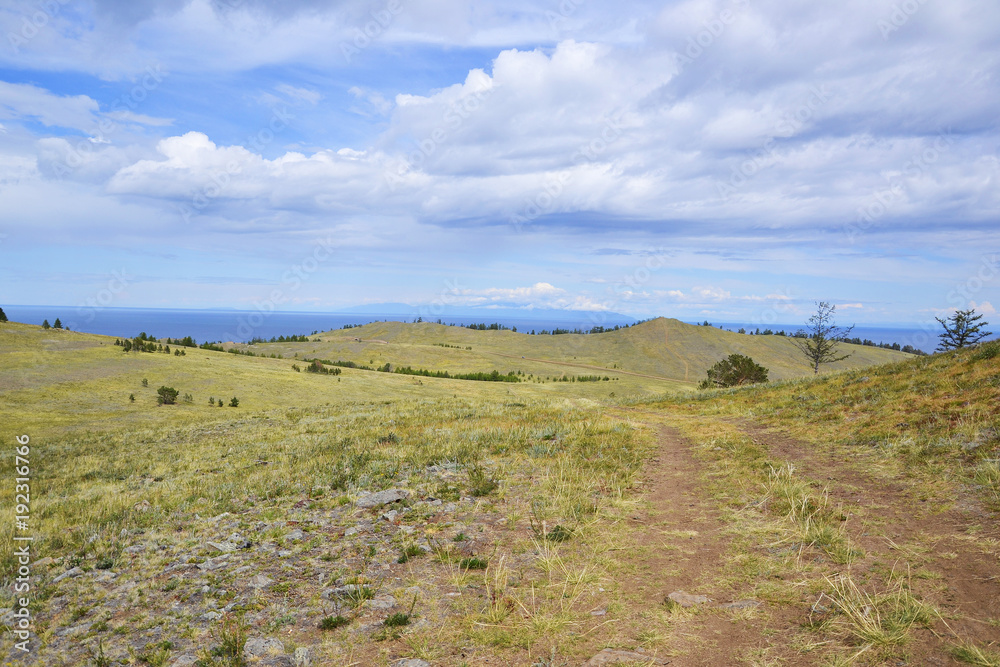 great white cloud green meadow and cape, road, mountains in the background and the blue water of the concept of idyllic Lake Baikal Olkhon Khuzhir town