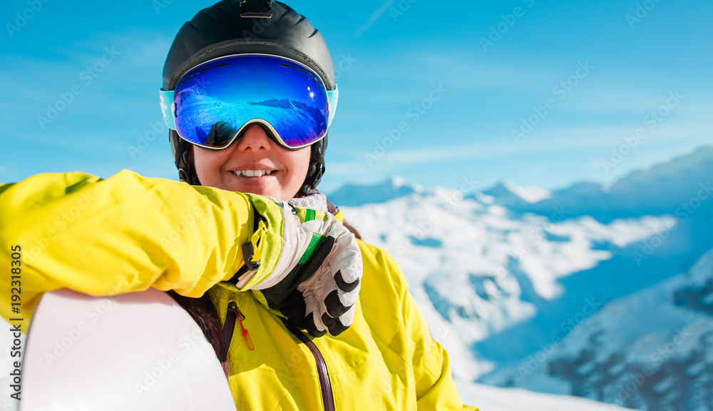 Image of smiling girl in helmet and mask with snowboard on background of snowy hills