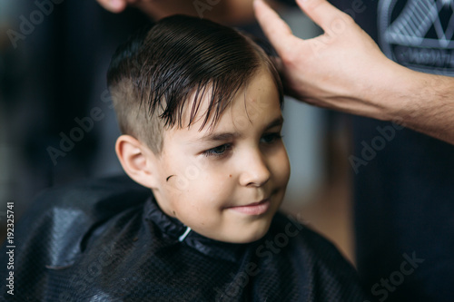 The boy getting haircut by scissor in barbershop. Barber use scissor