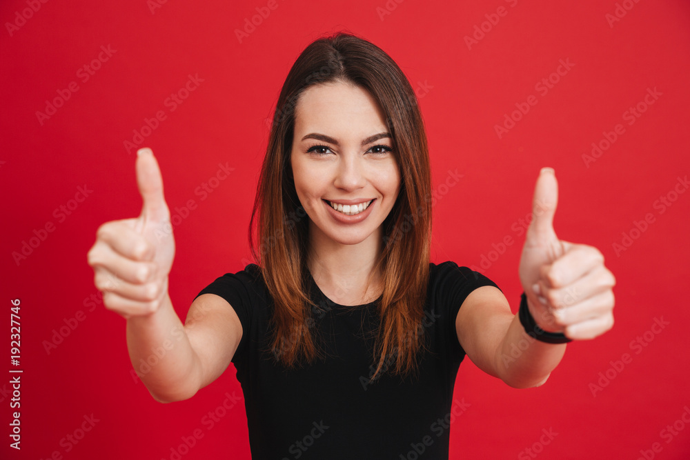 Portrait of adult brunette woman looking at camera with smile and showing thumbs up, isolated over red background Portrait of adult brunette woman looking at camera with smile and showing thumbs up, isolated over red background