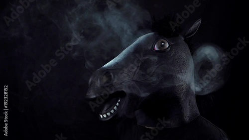 Man in the mask of a horse in smoke in slow motion on a black background photo