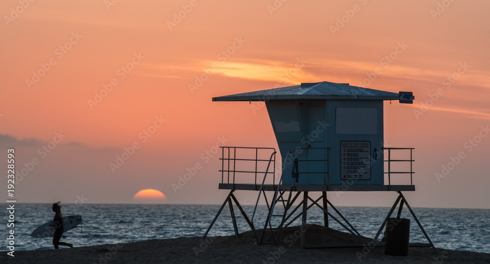 Surfer running past lifeguard tower at sunset on Huntington beach in southern California