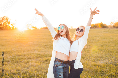 Two lovely girls are waving hands on a field at sunset.
