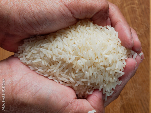 Woman hands holding white raw rice over brown wooden background