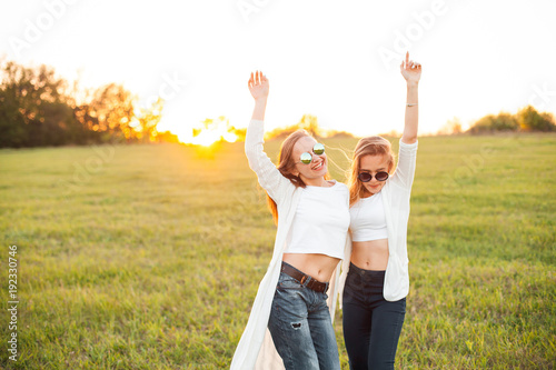 Two charming women are dancing on the field at the sunset.