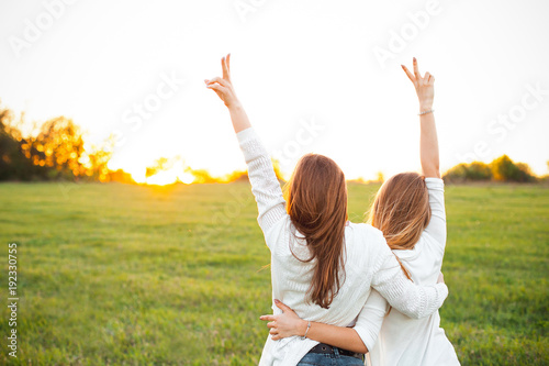 Two women in white sweaters are looking on the sunset. Best friends