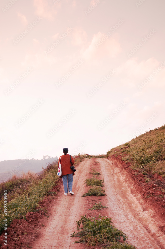 Young woman walkin on dirt path country road on the hill at evening sunset