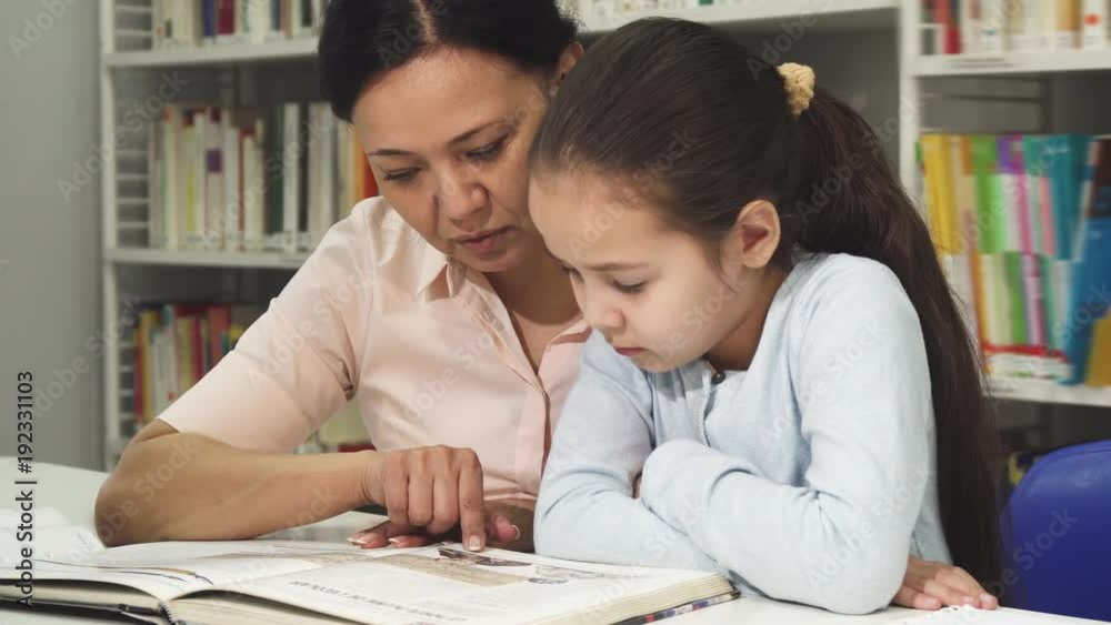 Asian mature woman reading a book with her cute litlle daughter Asian mature woman reading a book with her cute litlle daughter