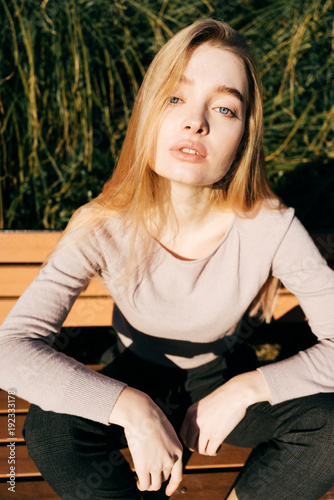 young beautiful model girl with blond hair with blue eyes sitting on a bench, posing