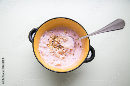 Breakfast yogurt with granola in a yellow bowl  and spoon on a white background