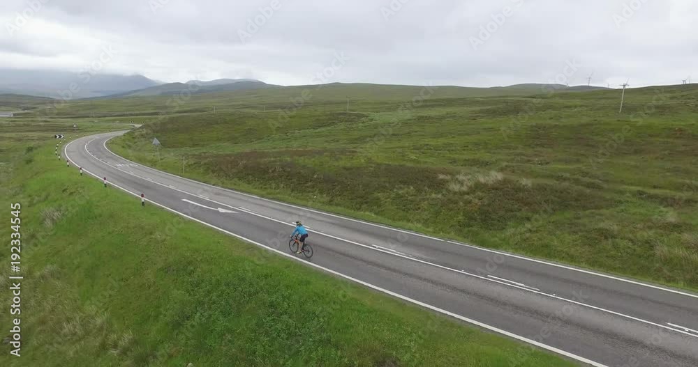Aerial shot following a male cyclist on country road on a beautiful day Aerial shot following a male cyclist on country road on a beautiful day