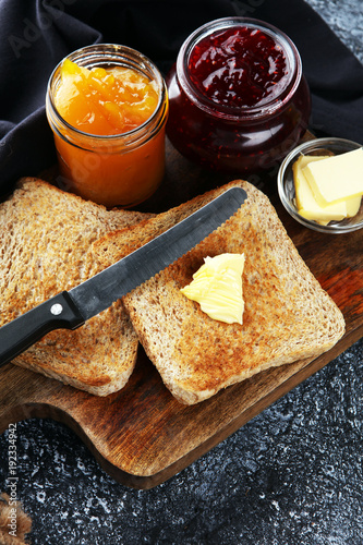 Toast bread with homemade strawberry jam and orange marmalade on rustic table served with butter for breakfast or brunch