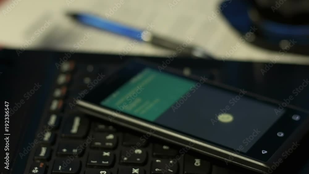 Cheap mobile phone lying on laptop keyboard in office and there is incoming call Cheap mobile phone lying on laptop keyboard in office and there is incoming call