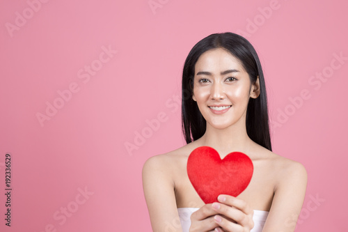 Portrait of Beautiful Asian Woman holding red heart symbol. Beautiful Woman looking to camera. People with Youth and Skin Care Concept. isolated on pink background.