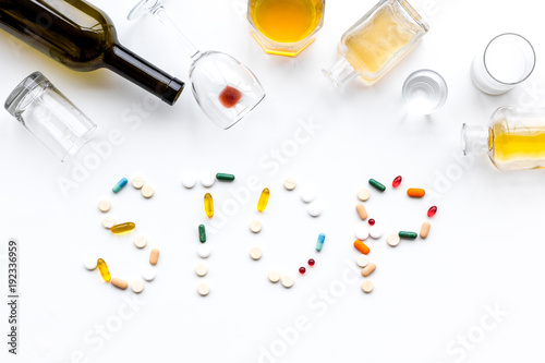 Stop alcohol. Word stop lined with pills near glasses and bottles on white background top view