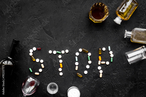 Stop alcohol. Word stop lined with pills near glasses and bottles on black background top view copy space