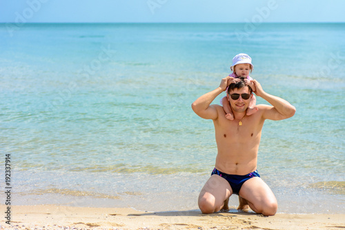 Young father in glasses sits on the beach with his daughter