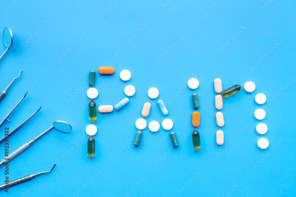 Toothache, dental pain. Fear of dental treatment. Word pain lined with pills near dentist tools. Blue background top view copy space Toothache, dental pain. Fear of dental treatment. Word pain lined with pills near dentist tools. Blue background top view copy space