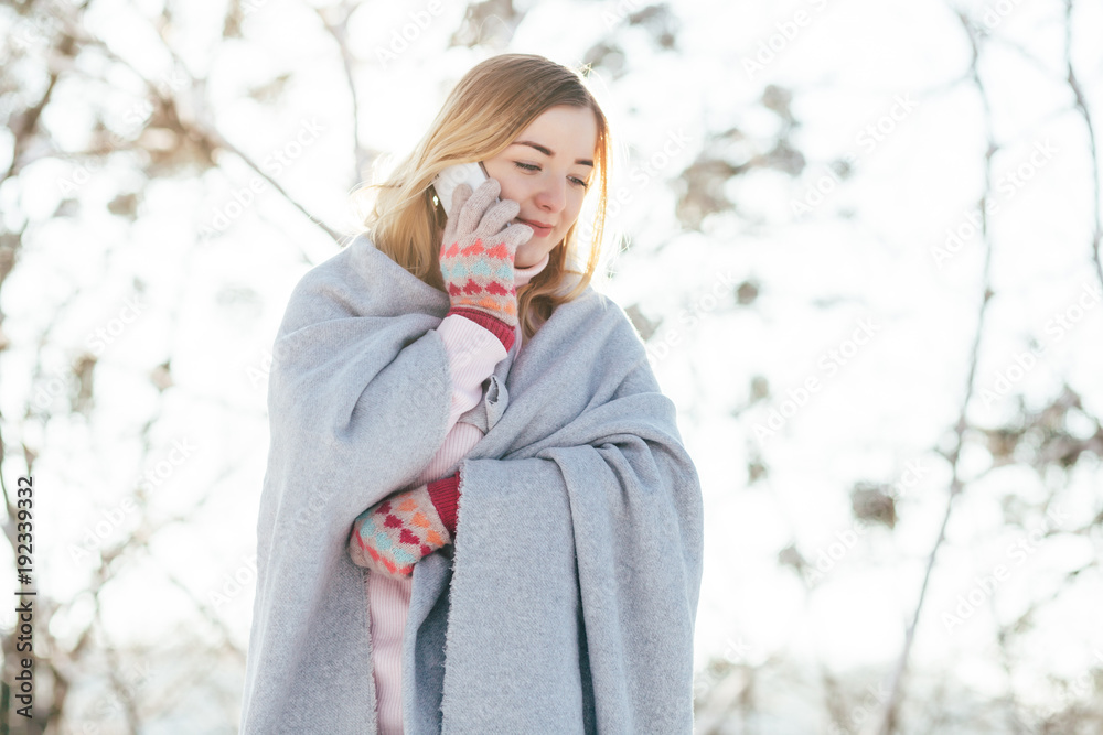 Young caucasian attractive blonde girl in pink sweater and knitted scarf holds smartphone in winter park outdoor Young caucasian attractive blonde girl in pink sweater and knitted scarf holds smartphone in winter park outdoor