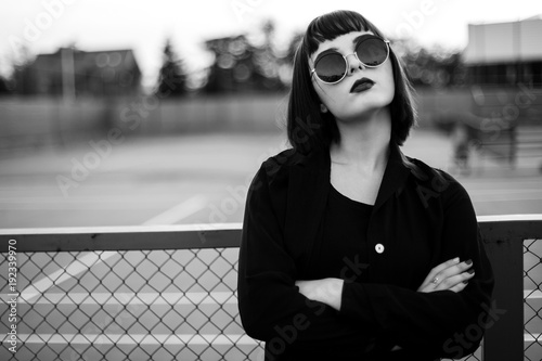 Pretty young girl stands on the background of a fence. Black and white