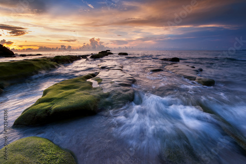 Long expose seascape with rocks covered by green moss and waves trails. soft focus due to slow shutter.