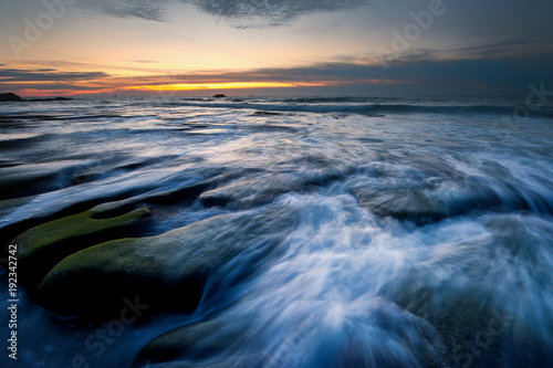 unique coastal rocks formation by the beach with waves trails during sunset.