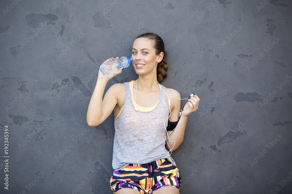 Young athletic woman drinking water by the wall