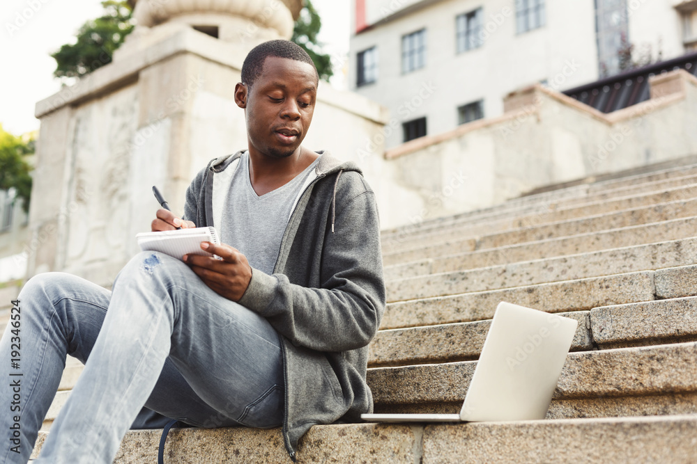 Concentrated african-american student studying with laptop and notebook outdoors