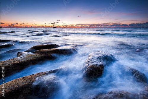 scenic view of sunset seascape with rocks covered by green moss on the ground. image contain soft focus due to slow shutter. © udoikel09