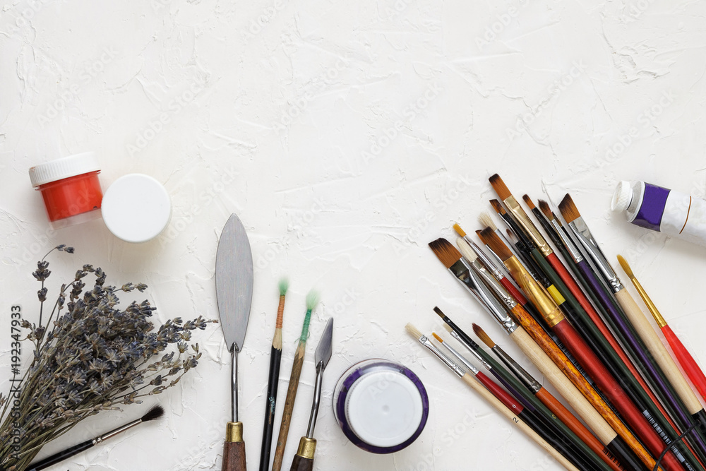 Fototapeta premium Professional brushes for artists, palette knives, colorful paints and dried lavender branches lie on a white canvas