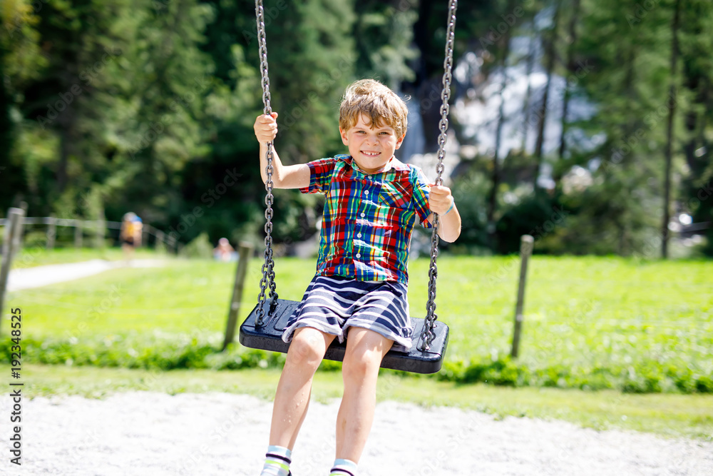 Funny kid boy having fun with chain swing on outdoor playground during rain Funny kid boy having fun with chain swing on outdoor playground during rain