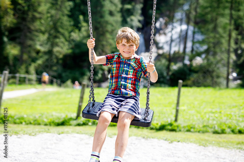 Funny kid boy having fun with chain swing on outdoor playground during rain © Irina Schmidt