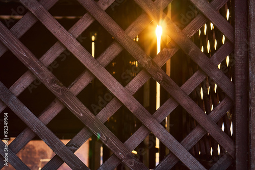 Natural background grille made of wooden slats. Element for the design of arbors, verandas and other wooden structures. The rays of the setting sun make their way through the bars.