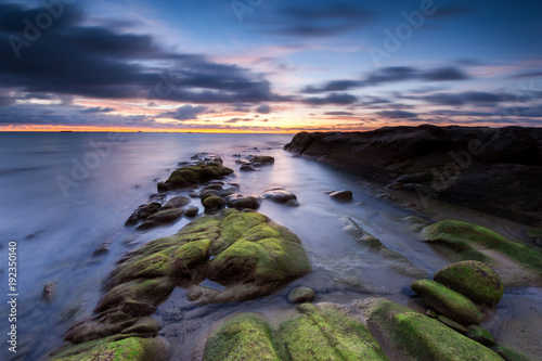 sunset seascape with natural coastal rocks by the beach.