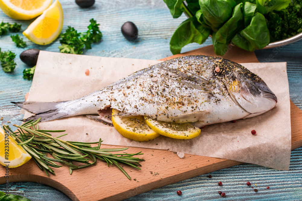 Cooking Raw Dorado Fish with Spinach, rosemary, olives, Herbs, Spices and Lemon closeup on Wooden Cutting Board on an aquamarine background Cooking Raw Dorado Fish with Spinach, rosemary, olives, Herbs, Spices and Lemon closeup on Wooden Cutting Board on an aquamarine background