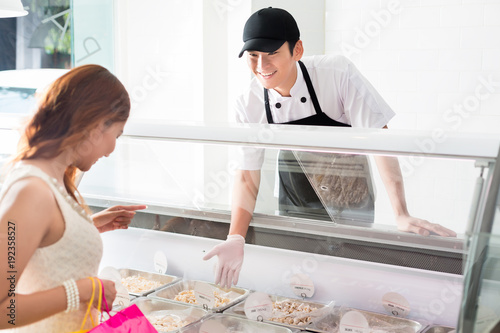 Young deli assistant serving a customer pointing to a selection of food in a glass counter as she tries to make a decision