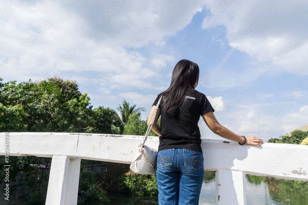 Back view of young adult woman wearing black shirt standing on old bridge and look at the sky with copy space for text., nature concept. goal concept. decision concept.