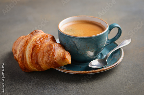 Cup of fresh coffee with croissant on concrete background, selective focus.