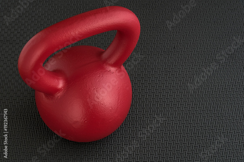 Close up of a red kettle bell on a textured black floor
