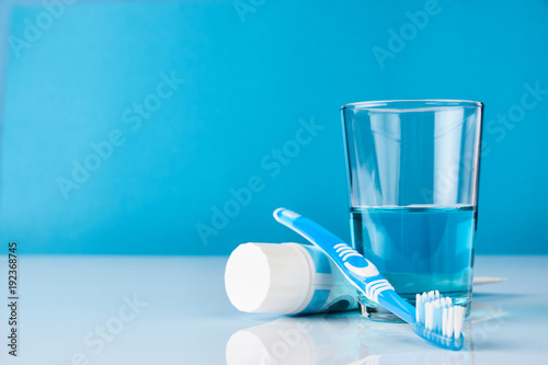 A blue toothbrush with toothpaste and glass of blue mouthwash on blue background with copy space, close-up. Dental oral hygiene concept photo