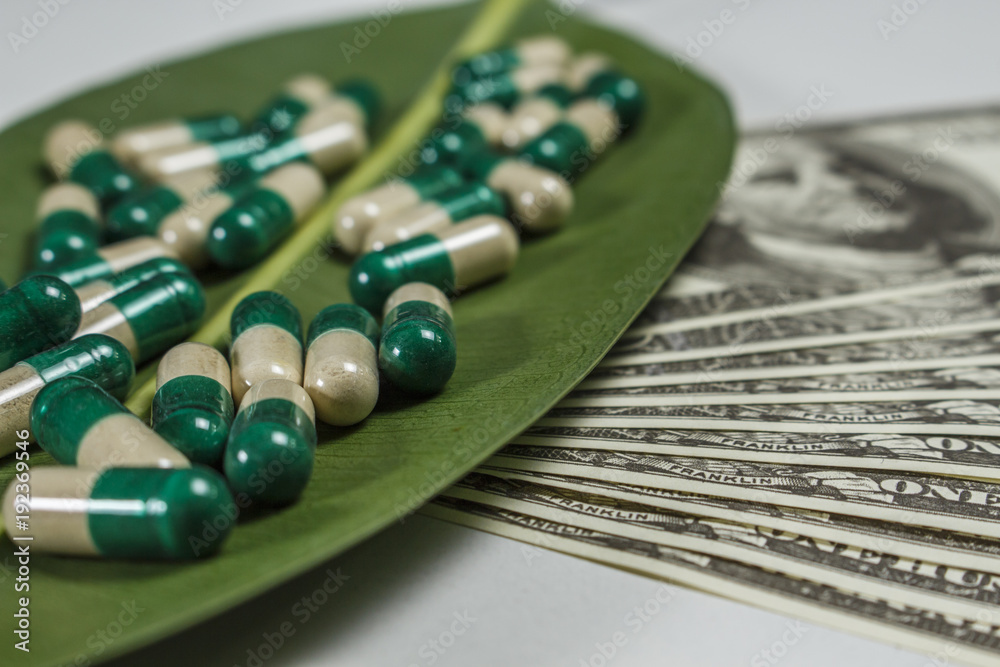 Pile of capsules on green leaf near dollars Pile of capsules on green leaf near dollars