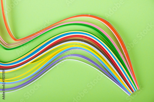 Rainbow colored quilling paper laying on waves on green background