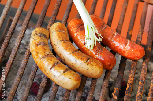 Close up of grilling sausages on barbecue grill with a long white onion. BBQ in the garden. Bavarian sausages