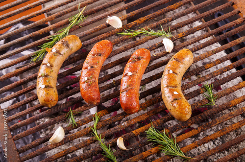 Top view of four grilling sausages on barbecue grill with some species. BBQ in the garden. Bavarian sausages photo