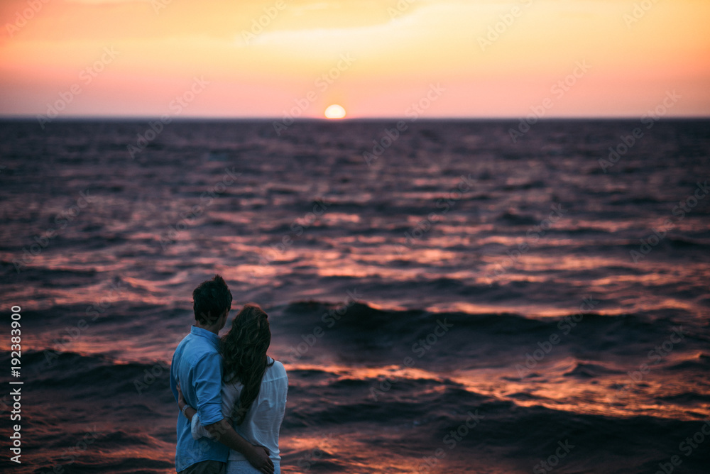 A romantic photo on which a couple in love stands on the seashore and admires the beautiful sunset