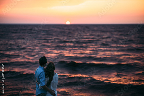 A romantic photo on which a couple in love stands on the seashore and admires the beautiful sunset