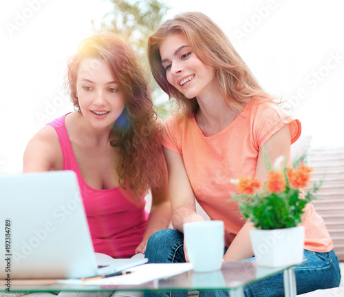 two student girls looking at laptop screen while sitting on the couch.