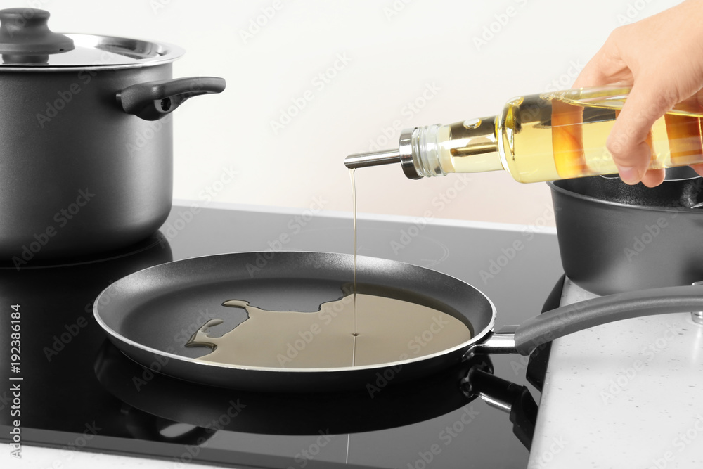 Woman pouring cooking oil from bottle into frying pan on stove
